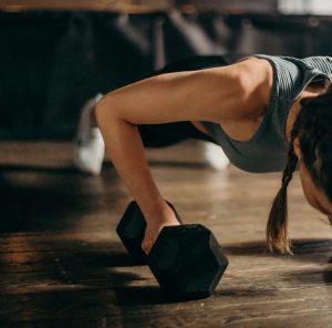 Girl doing pushups incorporating dumbells in each hand  